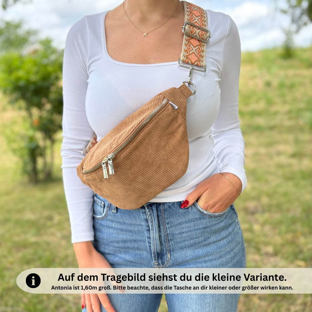 Kleine braune Bauchtasche aus Cord, crossbody getragen von Frau in weißem Oberteil und Jeans – kompakte Größe gut erkennbar, Model ist 1,60 m groß