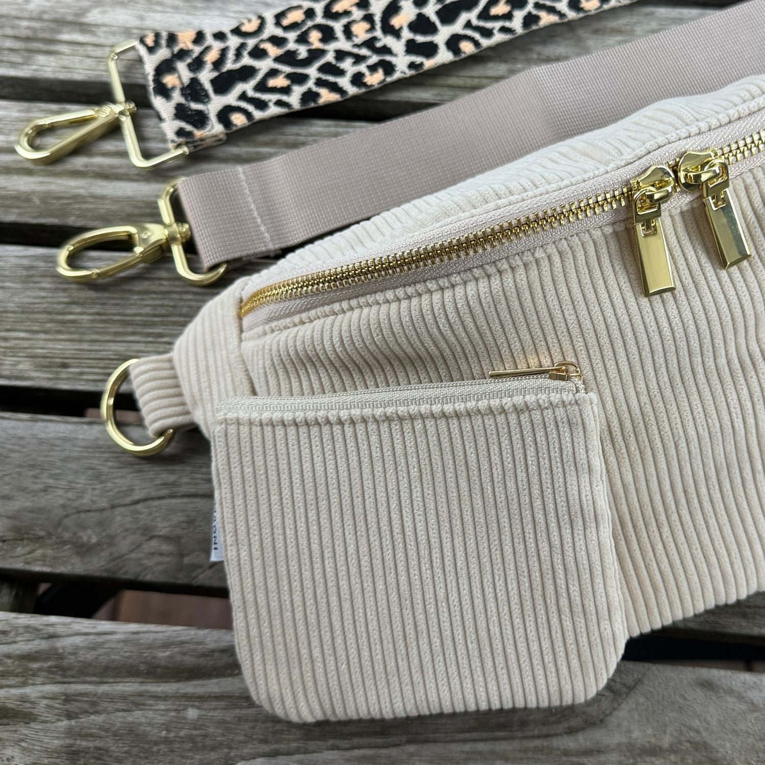 Nahaufnahme von Cord Bauchtasche mit Cord Geldbörse in der Farbe Beige. Im Hintergrund links oben im Bild ist ein einfarbiger und Leo-Taschengurt zu sehen.
