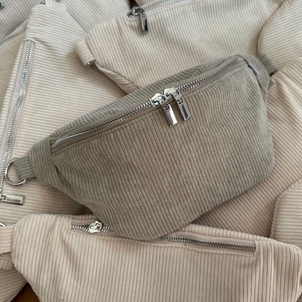 Cord Szene: grüne Cord Bauchtasche liegt in einem Meer von beigen Cord Bauchtaschen.