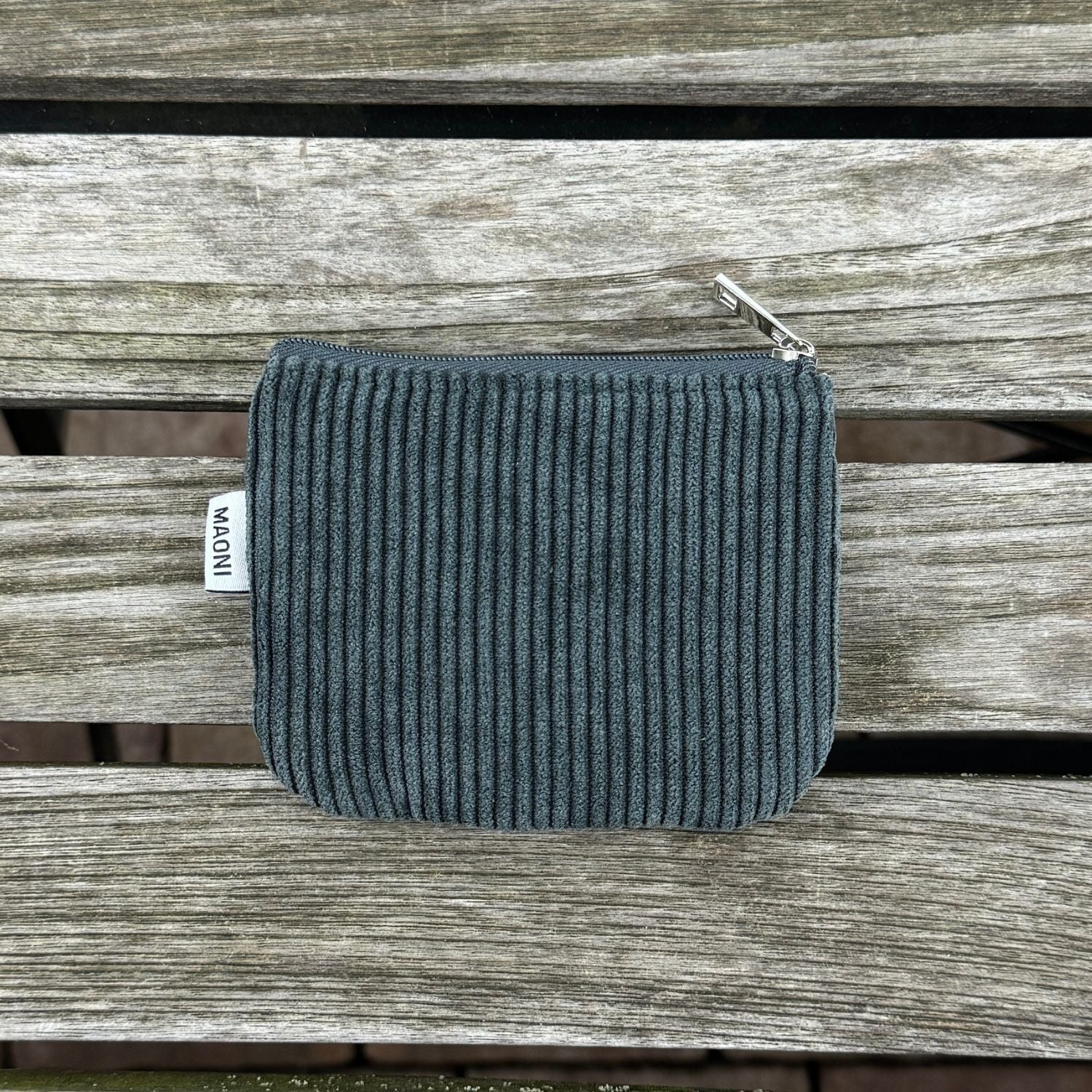 Dunkelgraues Cord-Etui mit silbernem Reißverschluss, auf einem Holztisch liegend – praktisches und stilvolles Accessoire.