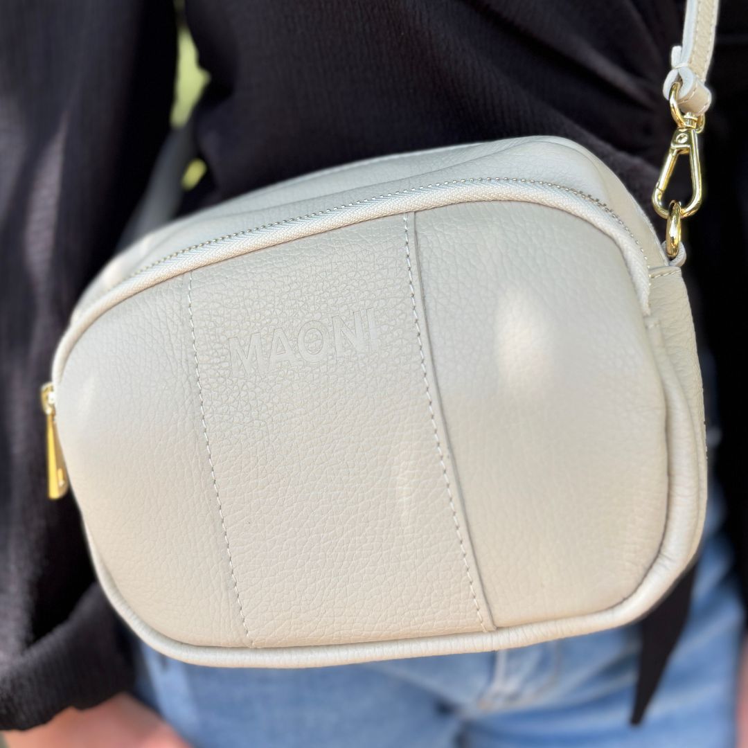 Nahaufnahme einer beigefarbenen Tasche mit goldfarbenem Verschluss und dezenter MAONI-Prägung auf der Vorderseite