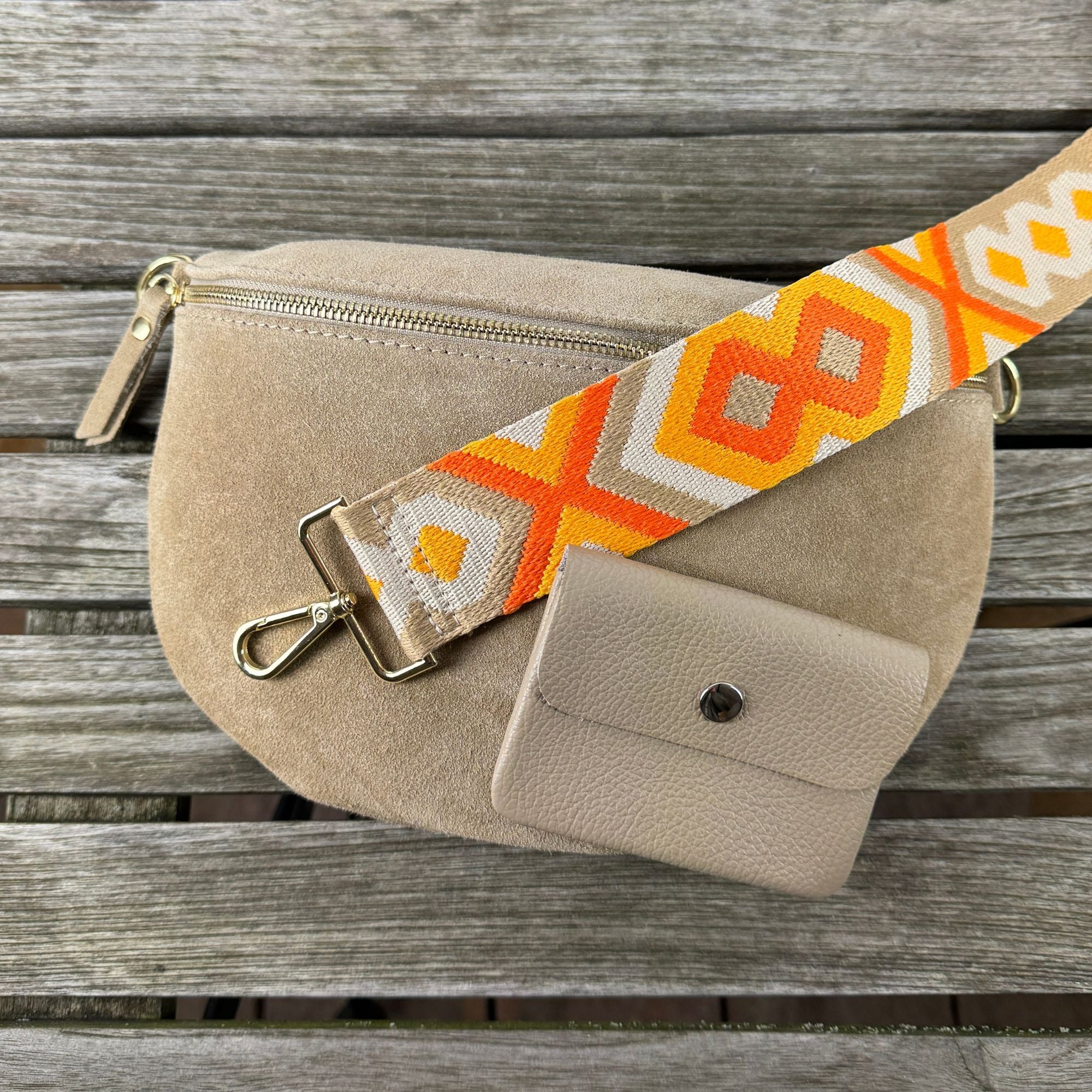 Orangefarbener Gurt mit goldfarbenem Verschluss kombiniert mit taupefarbener Wildledertasche und passender Leder-Geldbörse – stilvolles Accessoire-Set.