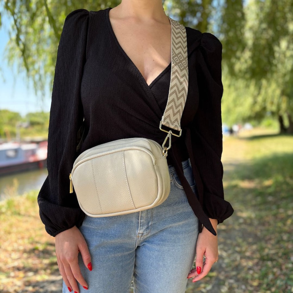 Beigefarbene Crossbody-Tasche mit auffälligem gezacktem Schultergurt – von einer Frau lässig über der Schulter getragen