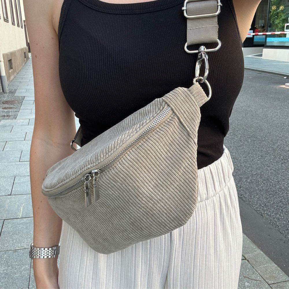 Praktische Bauchtasche aus Cord mit verstellbarem, auswechselbarem Gurt. Der Gurt ist einfarbig. Frau trägt Tasche in Innenstadt.