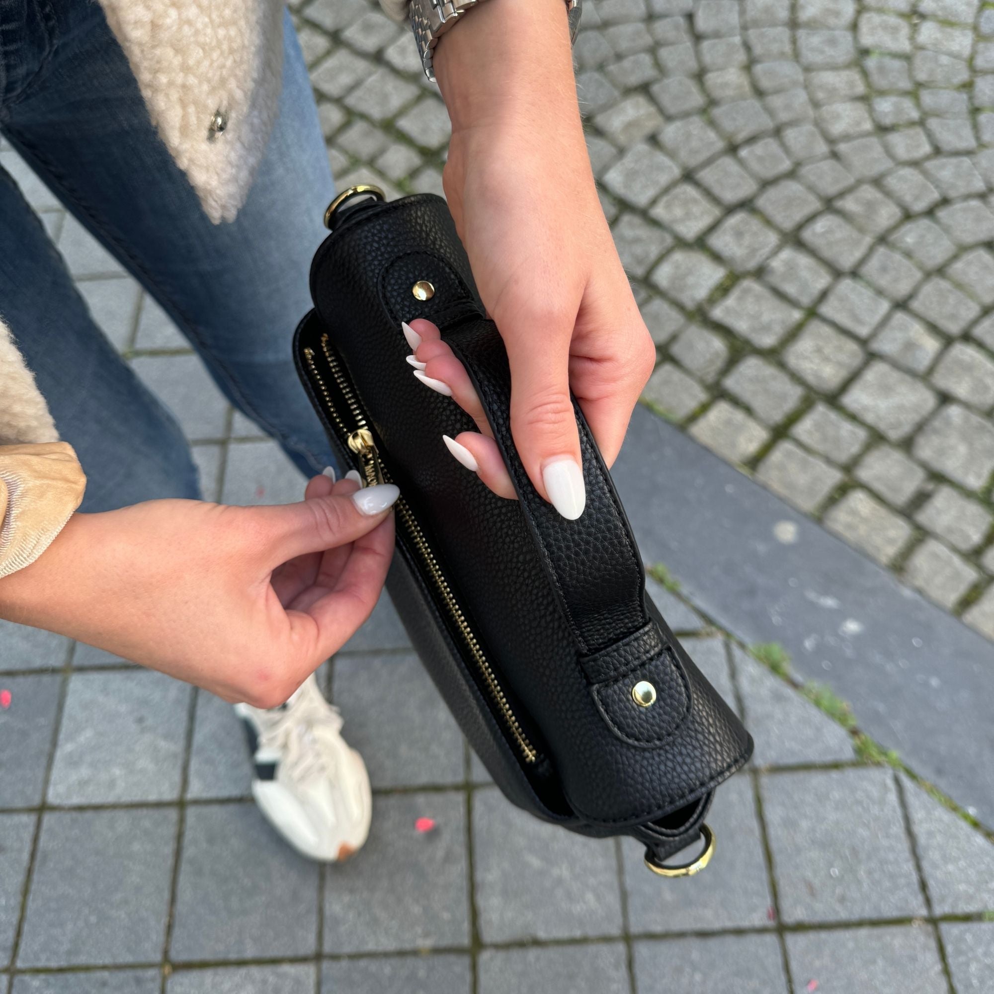 Frau trägt die schwarze Halfmoon-Tasche am kurzen Henkel und öffnet den Reißverschluss auf der Rückseite – aus der Vogelperspektive aufgenommen.