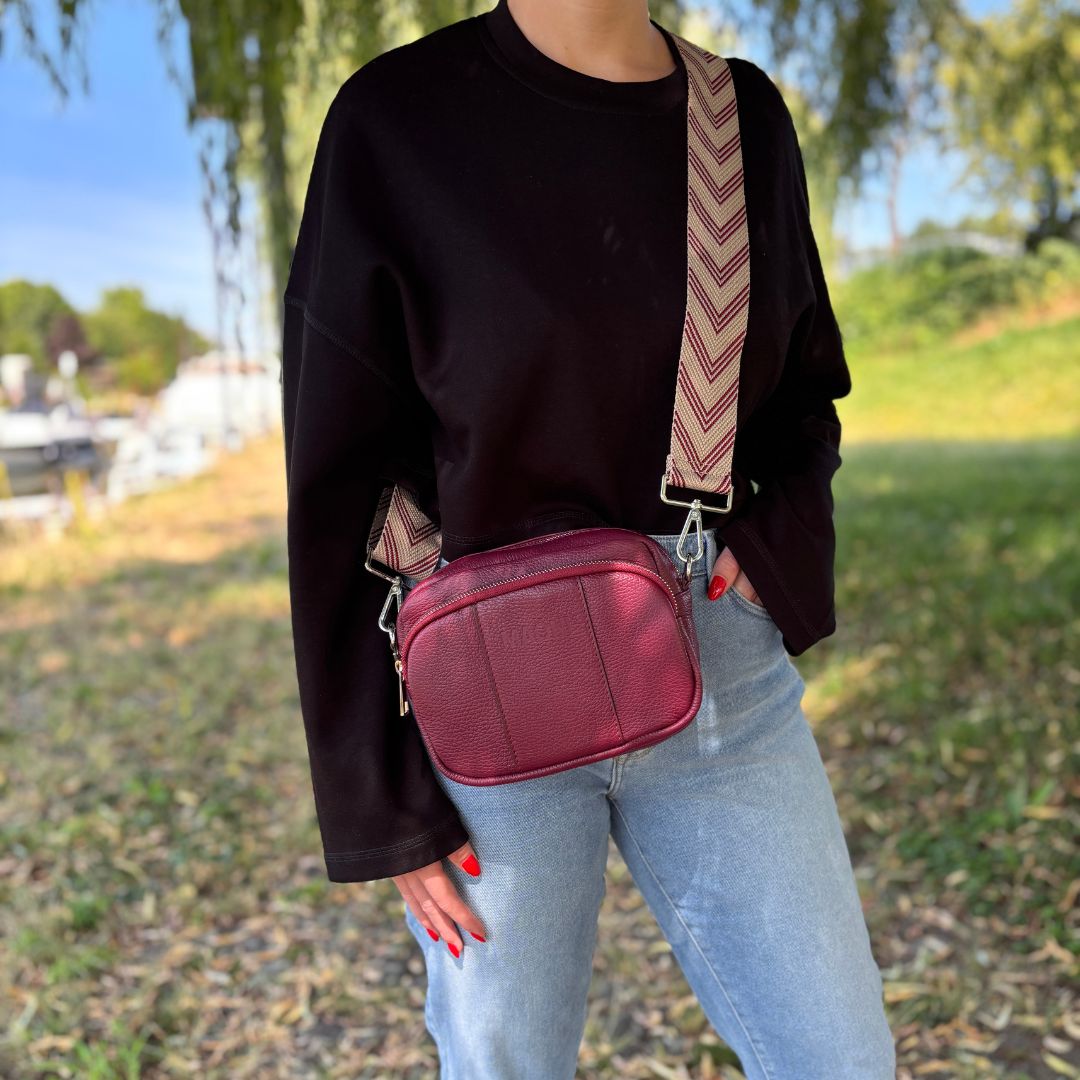 Crossbody-Bag in Burgunderrot mit breitem Muster-Gurt, getragen als modisches Statement-Piece