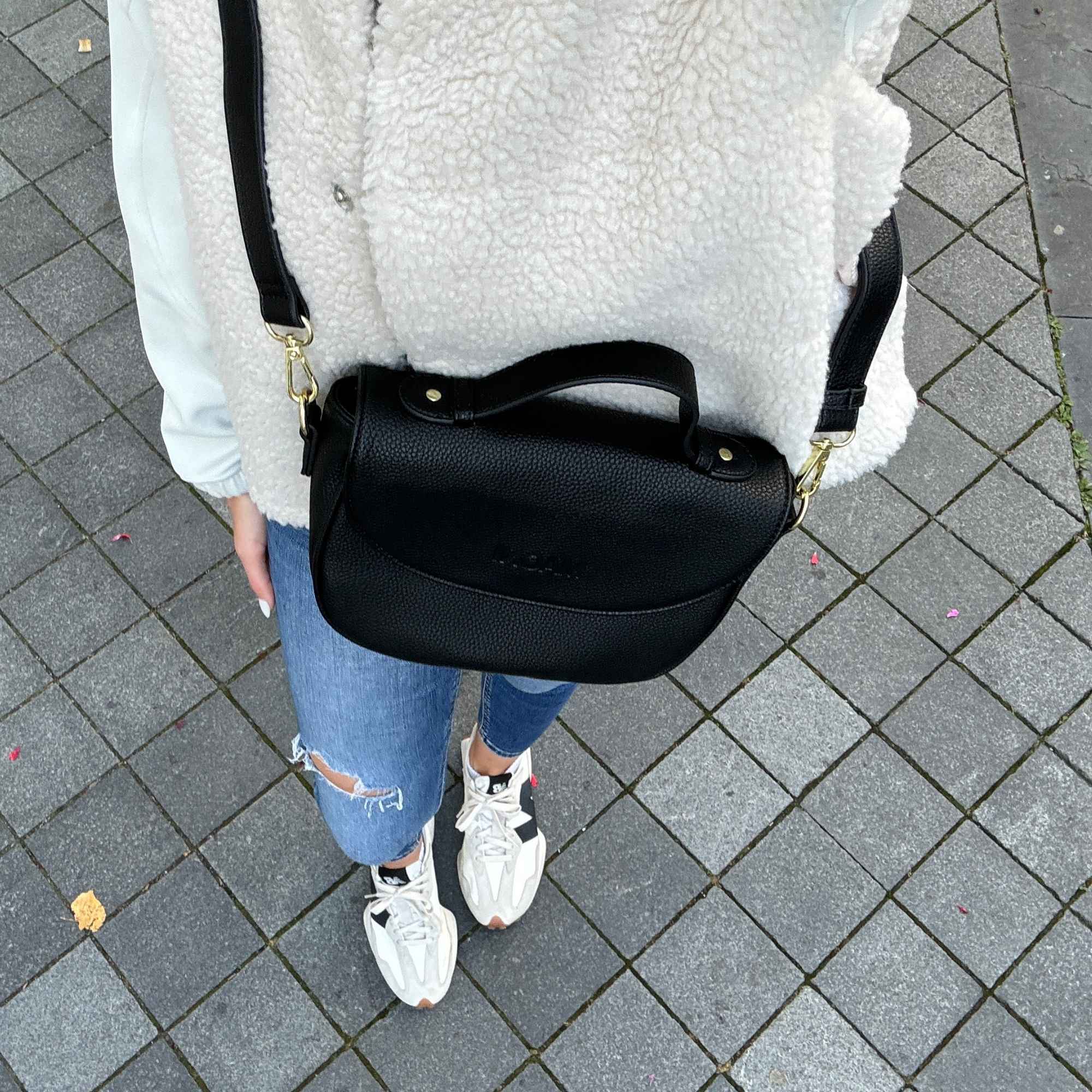 Frau präsentiert schwarze Halfmoon Tasche, auf beige Outfit und blauer Jeans – der Fokus liegt auf der Tasche.