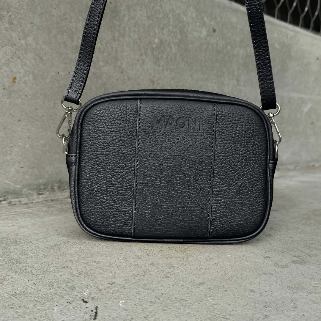 Schwarze Crossbody-Tasche mit einfarbigem Ledergurt auf Betongrund