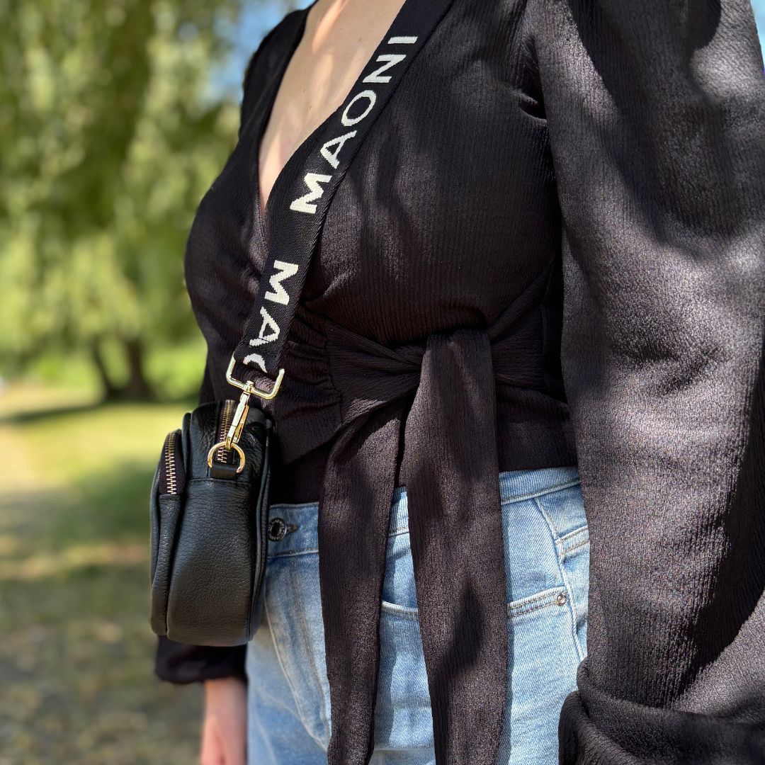 Seitenansicht einer schwarzen Crossbody-Tasche, getragen von einer Frau mit Wickelbluse – stilvoller Look für Alltag oder Büro